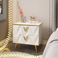 a white and gold dresser in a bedroom with lights on the wall behind it, next to a bed