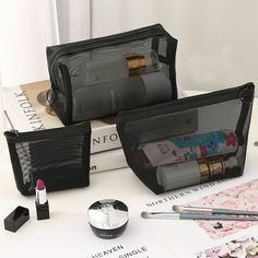 three black cosmetic bags sitting on top of a table next to books and makeup brushes