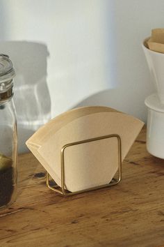 a napkin holder sitting on top of a wooden table next to a glass jar filled with liquid