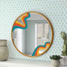 a round mirror sitting on top of a white shelf next to a potted plant