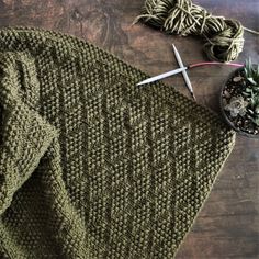 a green knitted sweater next to a potted plant and scissors on a wooden table