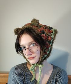 a woman wearing glasses and a knitted bear hat with green yarn around the brim