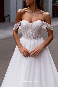 a woman wearing a white wedding dress standing on the street with her hands in her pockets