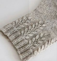 a close up of a knitted scarf on a white surface, with leaves and flowers in the middle