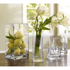 three glass vases with flowers and lemons in them sitting on a wooden table