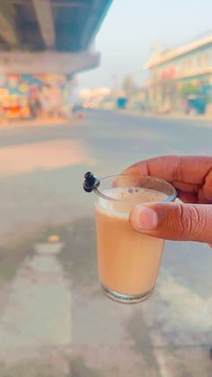 a hand holding a small glass filled with liquid and a black berry on the rim