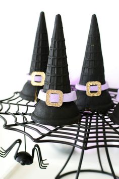 three black witches hats sitting on top of a wire rack with purple ribbons and gold buckles