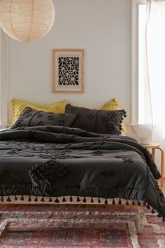 a bed with black comforter and pillows in a room next to a rug on the floor