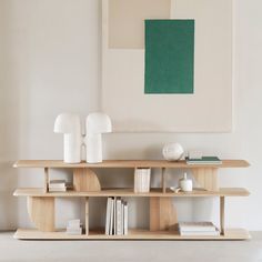 a wooden shelf with books and vases on it next to a wall mounted painting