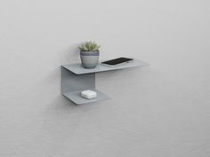 a small shelf with a phone and a plant on it next to a white wall