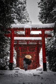 a person with a straw hat standing in front of a red gate covered in snow