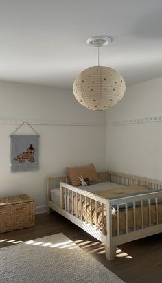 a white room with a bed, basket and lamp hanging from the ceiling in front of it