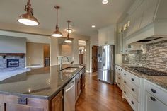 a large kitchen with an island and stainless steel appliances in the center, surrounded by wood flooring