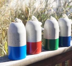 four different colored vases sitting on top of a wooden table next to tall grass