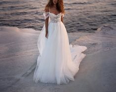 a woman in a wedding dress standing on the beach at sunset with her hair blowing in the wind