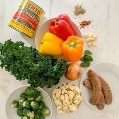 various vegetables and spices on a white counter top, including peppers, broccoli, carrots, cashews, peanuts