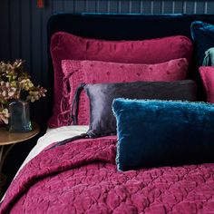 a bed covered in pink and blue pillows next to a table with flowers on it