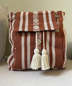 a brown and white striped purse with tassels on the front, sitting on a couch