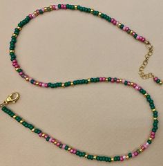 a beaded necklace with a gold clasp on a white table top, next to a pink and green bead