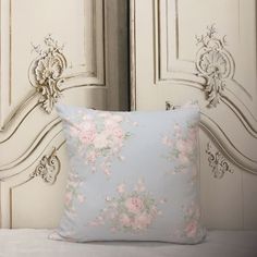 a blue pillow with pink flowers on it sitting on a bed next to a white door