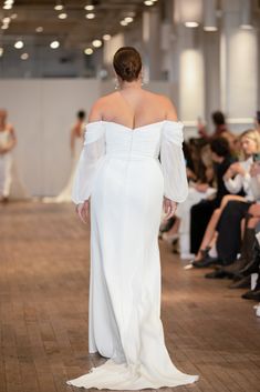 a woman in a white dress walking down a runway