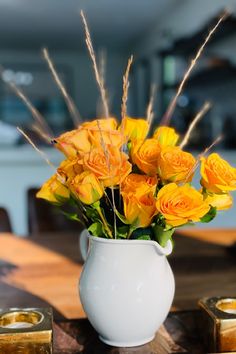 a white vase filled with yellow flowers on top of a wooden table next to candles