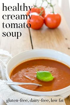 a bowl of tomato soup on a wooden table with tomatoes in the background and text overlay that reads healthy creamy tomato soup