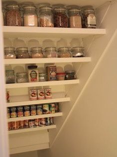 an organized pantry under the stairs with jars and other food items on shelves in it