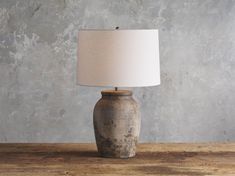 a table lamp sitting on top of a wooden table next to a gray stone wall