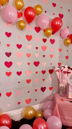 a room filled with lots of pink and red balloons next to a wall covered in hearts