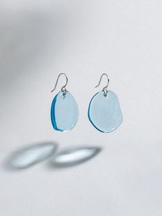 a pair of blue glass earrings on a white surface with two oval shaped drops hanging from them