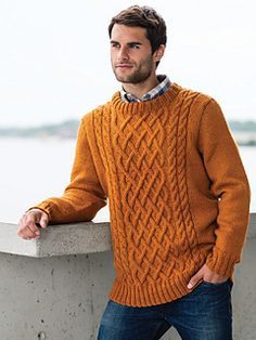 a man standing next to a cement wall wearing an orange cabled sweater and jeans