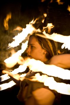 a woman sitting in front of a fire with birds flying over her head and arms