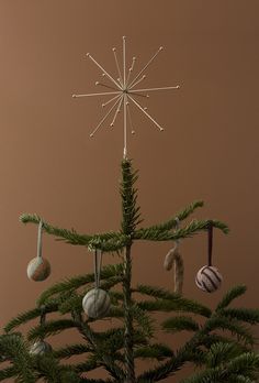 a small christmas tree with ornaments hanging from it's branches in front of a brown background