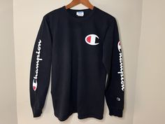 This is a black long sleeve athletic shirt featuring the Champion brand logo on the front and sleeves. It is made of 100% Cotton giving it a thick but comfortable feel. It is marked as a Men's Medium and fits True to Size. The shirt is in good vintage condition with no holes or tears - Please see photos.  Measurements laying flat: ~18 1/2 inches pit to pit ~24 inch sleeve ~27 inch length Sporty Long Sleeve T-shirt With Logo Print, Black Long Sleeve T-shirt With Ribbed Cuffs, Sporty Long Sleeve T-shirt For Winter, Sporty Long Sleeve Winter T-shirt, Sporty Winter Long Sleeve T-shirt, Fall Sports Long Sleeve T-shirt, Winter Sports Long Sleeve T-shirt, Long Sleeve Athleisure T-shirt For Streetwear, Black Athleisure Tops With Branding