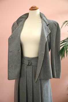 Size: Jacket size 4, Skirt size 6Material: 80% wool, 20% PolyesterLabel: Ellen TracyLadies 1970's light grey double-breasted suit features black piping,  stand up collar and original black buttons. Blazer and skirt are fully lined.  Skirt features pleats in both the front and back, side zipper and matching cloth belt.  Circa 1970's and in excellent vintage condition with no flaws.Measurements:Jacket:Bust-36 inchesAcross shoulders - 15 inchesLength - 22 inchesSleeve Length - 19 inchesSkirt:Waist Classic Wool Skirt Suit For Work, Classic Tailored Wool Skirt Suit, Classic Wool Long Sleeve Skirt Suit, Classic Winter Skirt Suit With Button Closure, Winter Classic Skirt Suit With Button Closure, Classic Winter Skirt Suit With Buttons, Tailored Skirt Suit For Fall Business Casual, Vintage Skirt Suit With Buttons For Office, Wool Skirt Suit For Tailoring