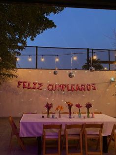 there is a table with flowers on it and lights strung from the wall behind it