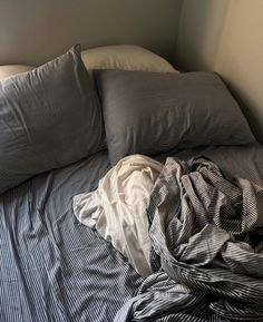 an unmade bed with striped sheets and pillows