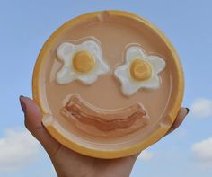 a person holding up a plate with two fried eggs on it's face and bacon in the middle