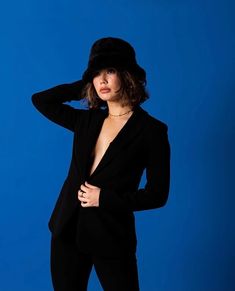 a woman in a black suit and hat posing for the camera with her hands on her hips