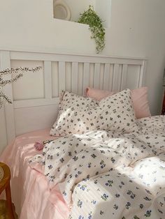 an unmade bed with pink sheets and flowers on the comforter, next to a plant