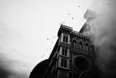 birds are flying in the sky above an old building