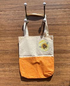 an orange and white tote bag with a bee on it sitting on top of a wooden floor