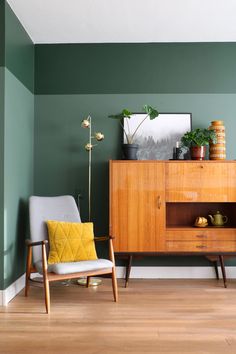 a living room with green walls and wooden furniture in the corner, along with potted plants