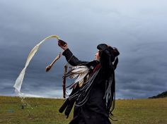 a woman dressed in black holding a long white feather and throwing it into the air