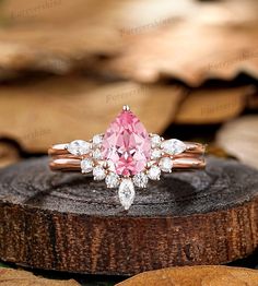 a pink diamond ring sitting on top of a piece of wood with leaves in the background