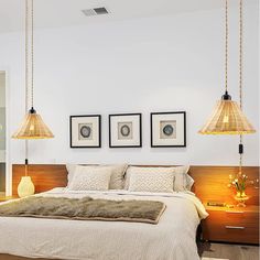 a bedroom with three lamps hanging from the ceiling and two pictures on the wall above the bed