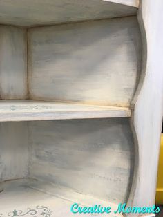 an empty shelf painted white with flowers on the top and bottom shelves, in front of a yellow chair