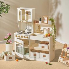 a doll house kitchen with wooden furniture and accessories on the floor in front of a potted plant