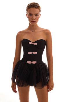 Cute and playful tutu black mini dress with pink bows. Featuring a strapless fitted drop-waist bodice with built-in cups and a hidden zip closure for structure and support. The soft pink bow appliqués and a puffy tulle skirt bring a quirky, almost theatrical vibe to the look.Details: Material: Khayal Fabric composition: 92% Polyester; 8% Elastan Sleeve style: Sleeveless Silhouette: Fitted Skirt length from waist: 5.9 inches / 15 cm Neckline: Sweetheart Back: Zip closure Lining: Mini-length skirt Party Corset Dress With Bow Straps, Strapless Coquette Mini Dress With Corset Back, Strapless Mini Dress With Corset Back In Coquette Style, Black Mini Length Corset For Cocktail, Strapless Coquette Corset For Party, Black Cocktail Dress With Bow Straps, Pink Coquette Corset For Party, Coquette Strapless Corset For Party, Black Mini Dress With Bow Straps